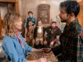 Ein Mann im karierten Bademantel hält die Hand einer Frau. Im Hintergrund sind mehrere historische Figuren zu sehen, die auf ein neues Abenteuer in "Ghosts Staffel 5" hindeuten.