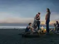 Die Gruppe von Mädchen am Strand bei einem Lagerfeuer. Die Stimmung ist nachdenklich, wie in "The Wilds Staffel 3".