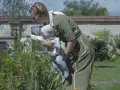 Frau mit Baby im Garten vor blühenden Blumen.