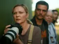 Kirsten Dunst mit Kamera, Teil der besetzung von Civil War, im Hintergrund unscharfe Personen.