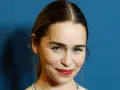 Emilia Clarke, bekannt für ihre Rollen in **filme und serien von Emilia Clarke**, lächelt charmant vor blauem Hintergrund.