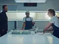 Ein Mann im Anzug beobachtet zwei Köche in einer Küche. Die Uhr zeigt 8:27. Szene aus "The Bear" Staffel 3.