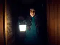 Frau mit Laterne im dunklen Flur einer Hütte. Ein Klopfen an der Kabinentür lässt sie innehalten.