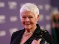 Dame Judi Dench, eine Ikone der Filme von Judi Dench, lächelt auf dem roten Teppich. Sie trägt eine schwarze Jacke, eine Diamantkette und hält eine glitzernde Clutch.