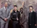 Die Besetzung von Jumanji: Dwayne Johnson, Nick Jonas, Kevin Hart und Jake Kasdan posieren vor einem Dschungel-Hintergrund.