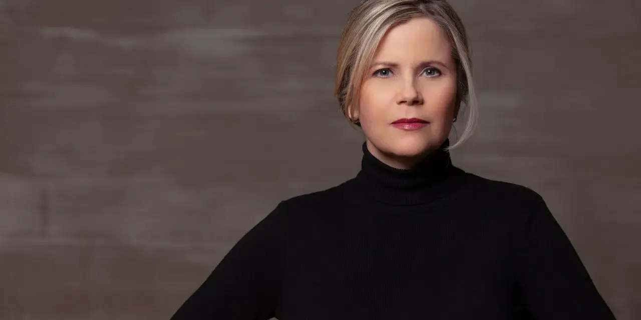 Porträt einer Frau mit blonden Haaren und einem schwarzen Rollkragenpullover. Sie könnte eine Schauspielerin sein, die in **Filme von Michaela Schaffrath** mitspielt.