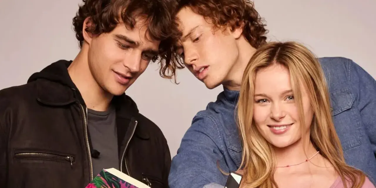 Die "Love Me, Love Me" Besetzung: Zwei junge Männer lesen ein Buch, während eine junge Frau lächelnd in die Kamera blickt.