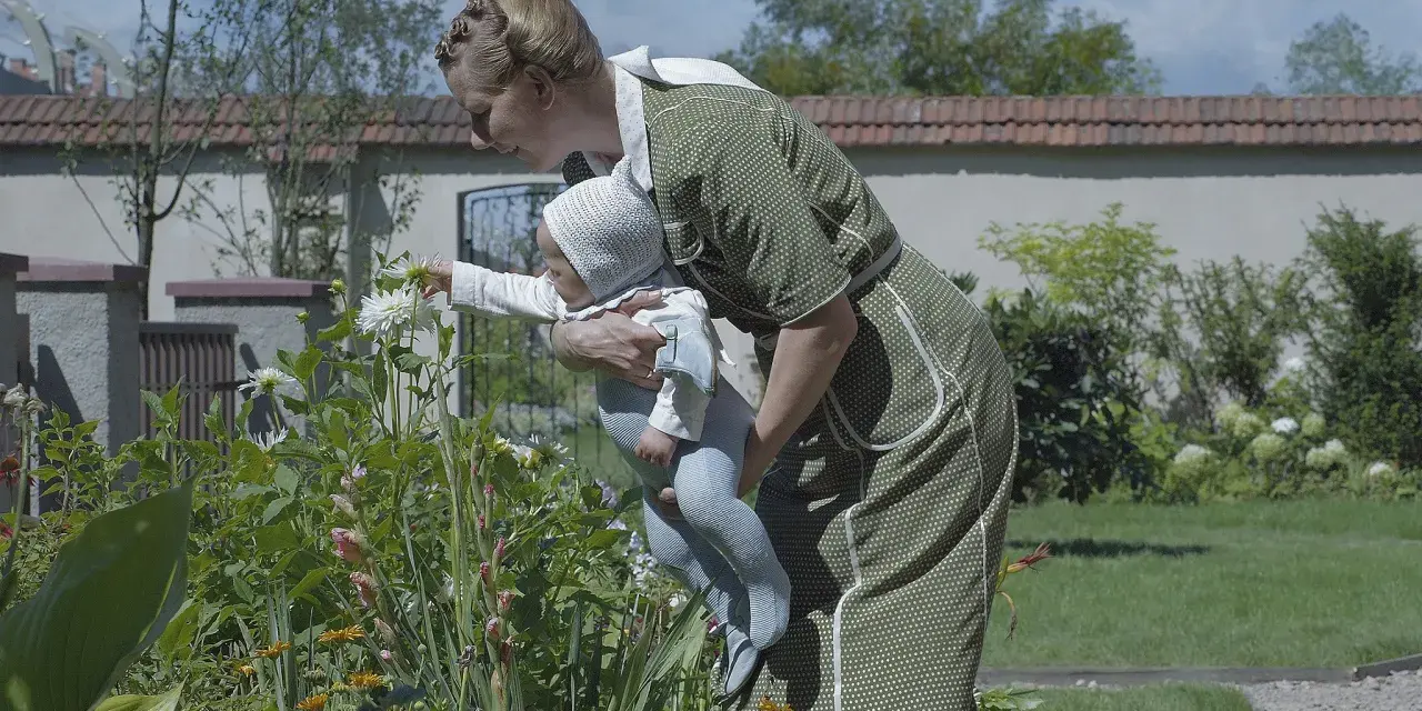 Frau mit Baby im Garten vor blühenden Blumen.