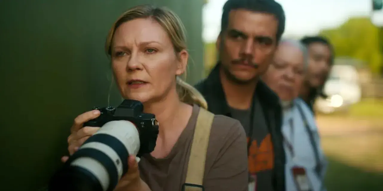 Kirsten Dunst mit Kamera, Teil der besetzung von Civil War, im Hintergrund unscharfe Personen.