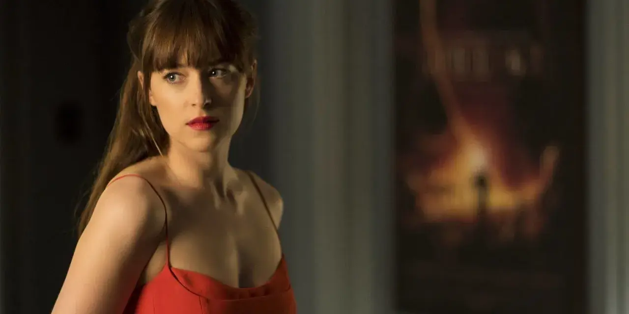 Dakota Johnson in einem roten Kleid, nachdenklich blickend. Ein Poster im Hintergrund deutet auf ihre Filme hin.