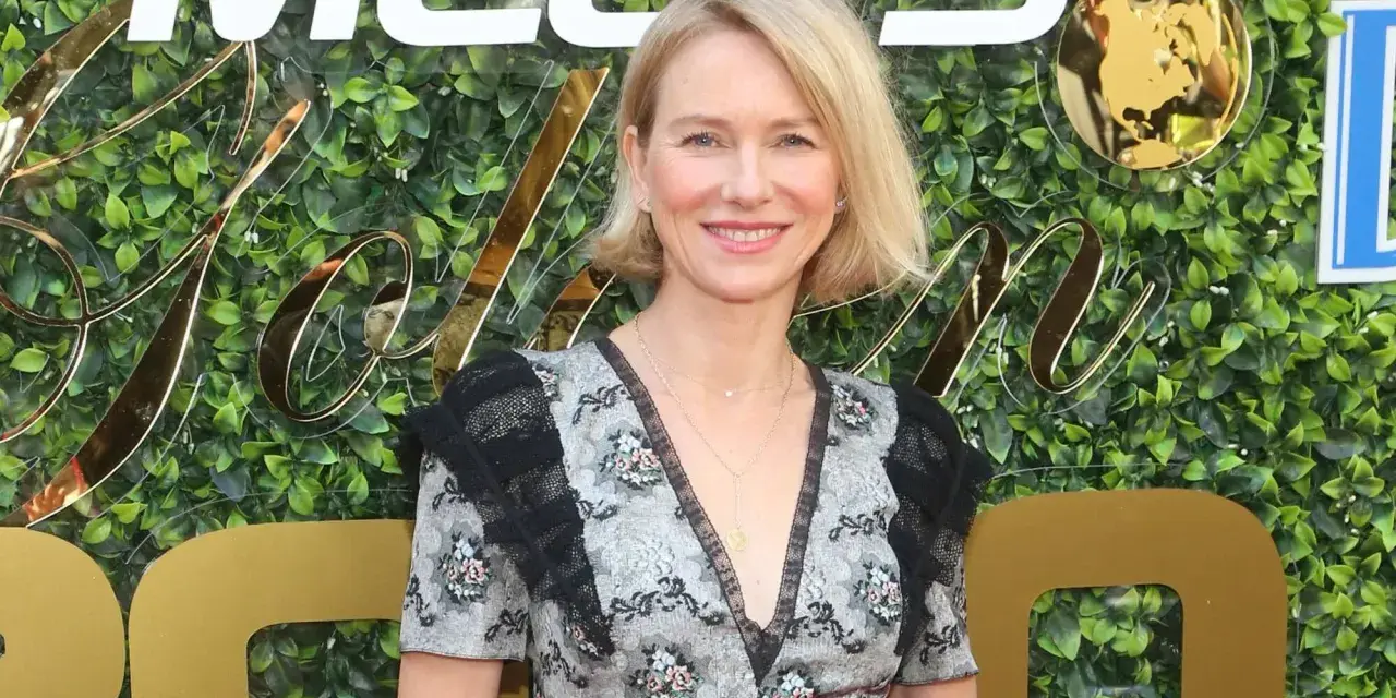 Naomi Watts lächelt vor einer grünen Wand mit goldenen Buchstaben. Sie trägt ein Kleid mit Blumenmuster. Ihre Filme sind oft spannend.