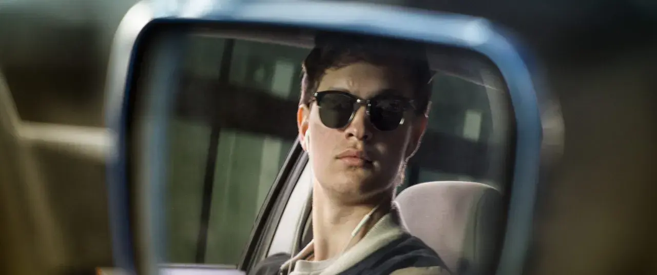 Ein junger Mann mit Sonnenbrille und Kopfhörern im Rückspiegel, der an die Besetzung von Baby Driver erinnert.