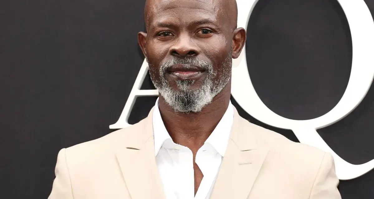 Djimon Hounsou, bekannt aus vielen Filmen, trägt einen hellbeigen Anzug und ein weißes Hemd.