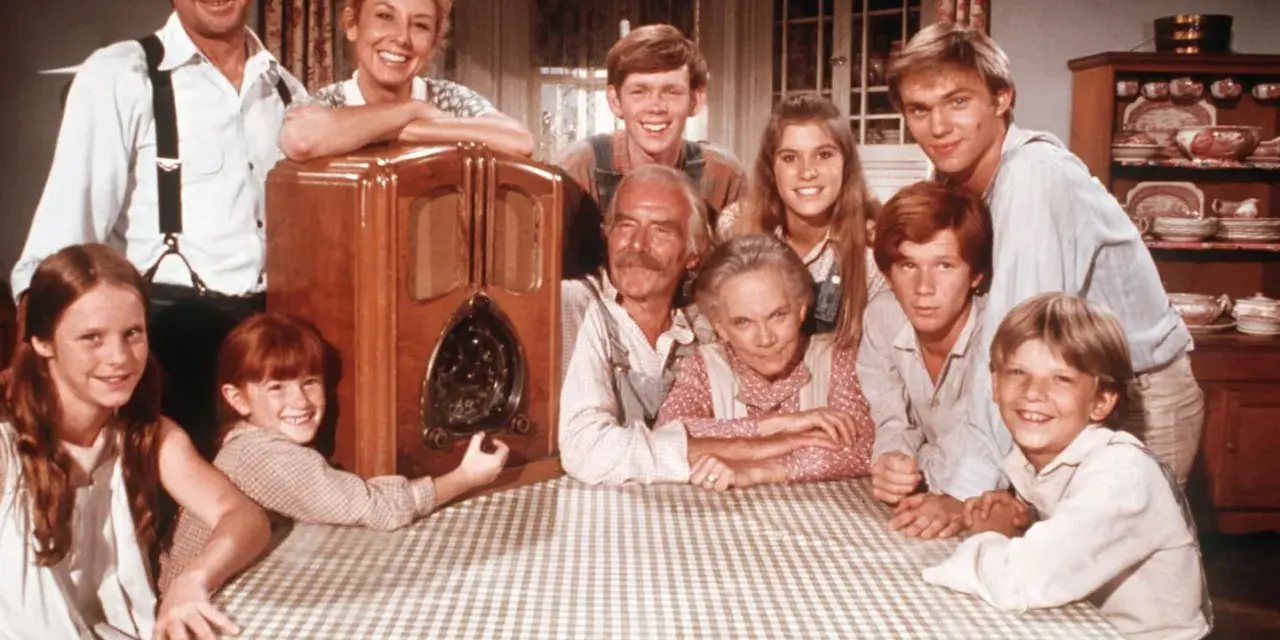Die Besetzung von Die Waltons versammelt sich um ein Radio. Die Familie lächelt fröhlich in die Kamera.