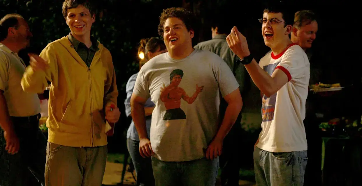 Die Besetzung von Superbad feiert eine Party. Michael Cera, Jonah Hill mit Bruce Lee T-Shirt und Christopher Mintz-Plasse lachen ausgelassen.