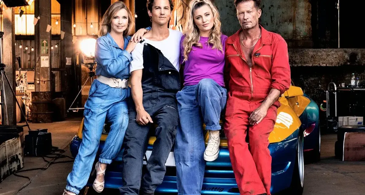 Die Besetzung von Manta Manta – Zweiter Teil: Til Schweiger, Tina Rönnau, Luna Schweiger und Moritz Bleibtreu posieren vor einem Auto in einer Werkstatt.