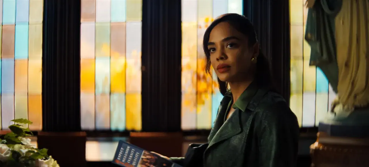 Tessa Thompson in einem grünen Mantel, mit einem Heft in der Hand, vor einem bunten Fenster. Ein Blick auf ihre Rolle in Filmen von Tessa Thompson.