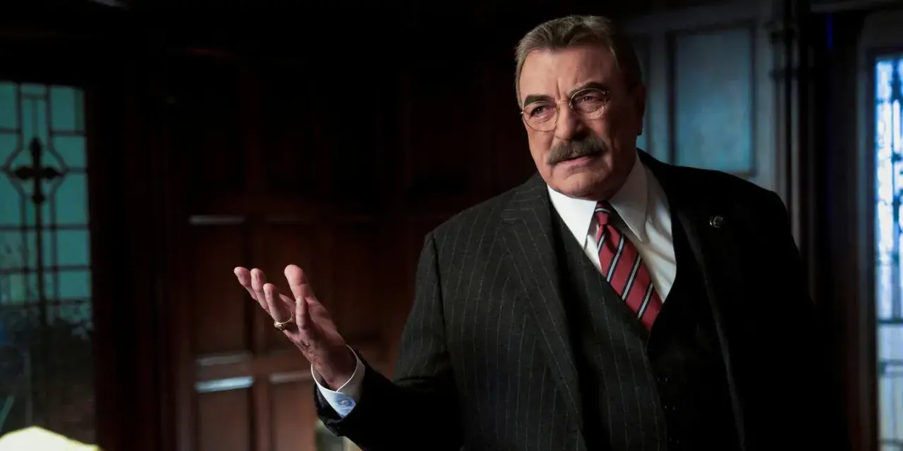 Frank Reagan in Blue Bloods Staffel 14, mit gestreiftem Anzug und Krawatte, erklärt etwas mit erhobener Hand.