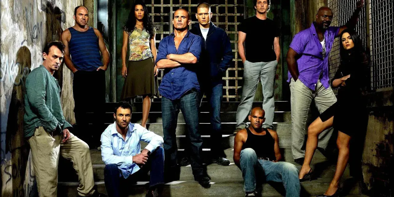 Die Hauptbesetzung von Prison Break posiert auf Treppen vor einem Gittertor.
