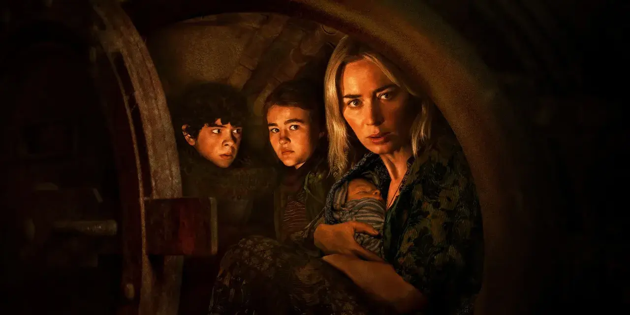 Die Besetzung von A Quiet Place: Eine Mutter hält ihr Baby, während ihre Kinder ängstlich in einem dunklen Versteck kauern.