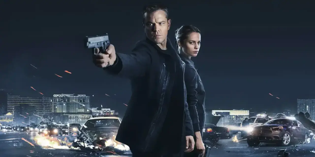 Jason Bourne und Alicia Vikander in Aktion. Ein Auto brennt, während Jason eine Waffe abfeuert. Die besetzung von Jason Bourne ist bereit für den Kampf.