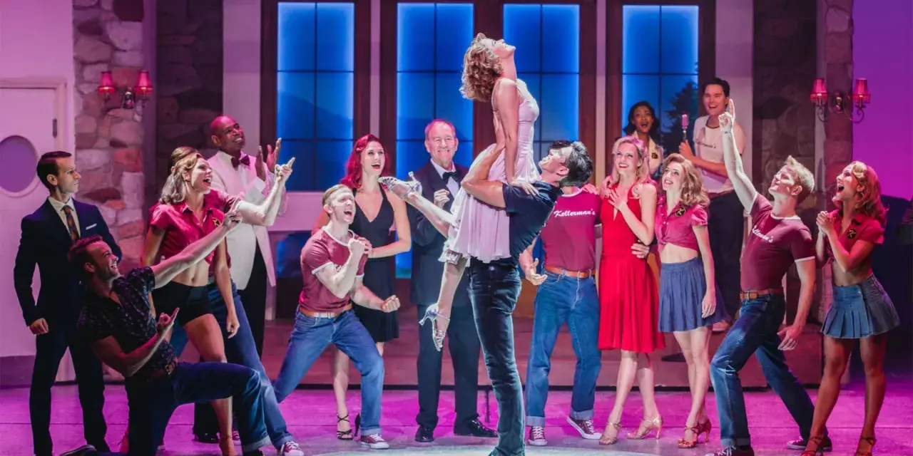 Die Besetzung von Dirty Dancing feiert auf der Bühne. Ein Mann hebt eine Frau in die Luft, während andere Tänzer jubeln.