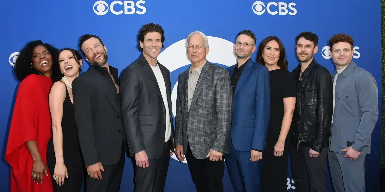 Die Besetzung von Navy CIS: Origins posiert auf einem blauen Teppich vor dem CBS-Logo.