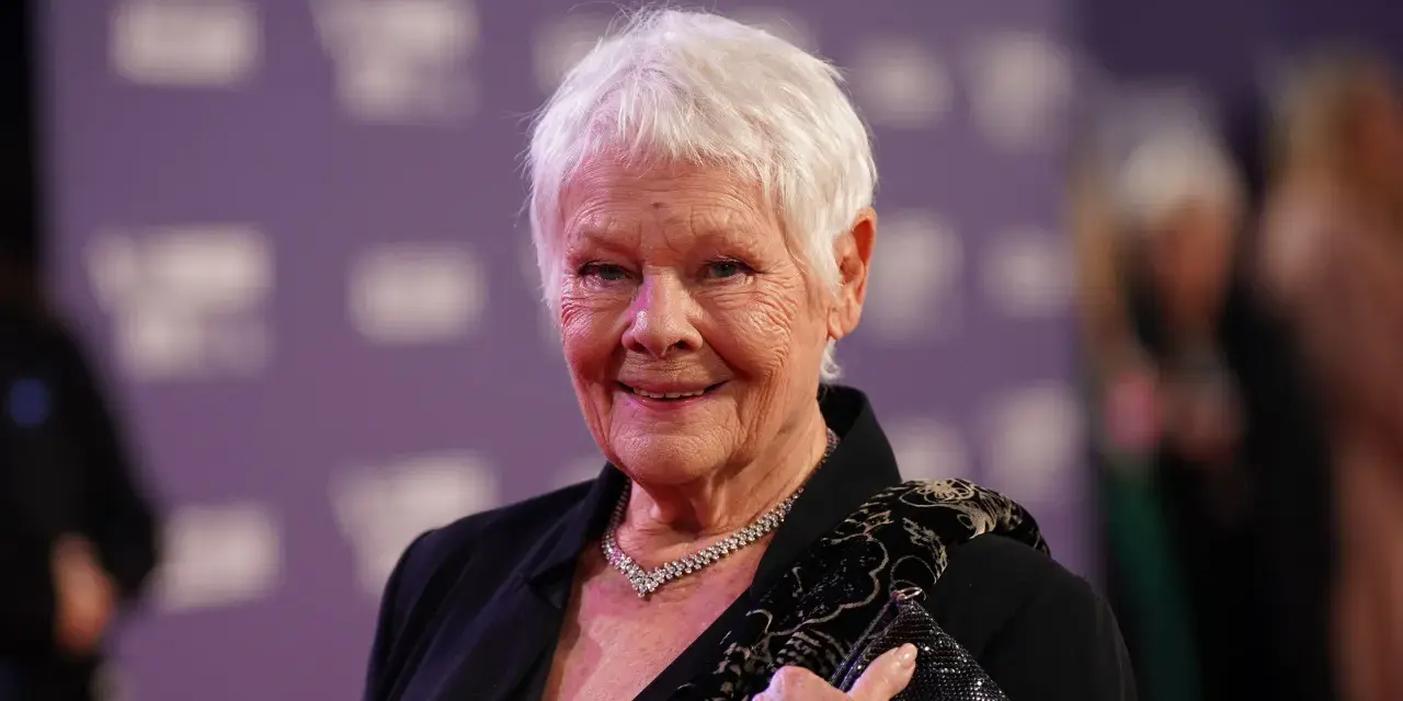 Dame Judi Dench, eine Ikone der Filme von Judi Dench, lächelt auf dem roten Teppich. Sie trägt eine schwarze Jacke, eine Diamantkette und hält eine glitzernde Clutch.
