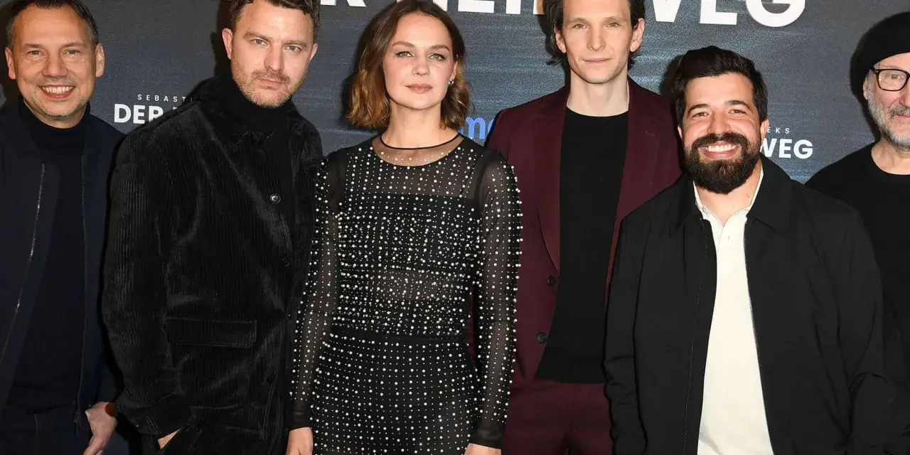 Das Ensemble des Films "Der heimweg" posiert lächelnd vor dem Banner.