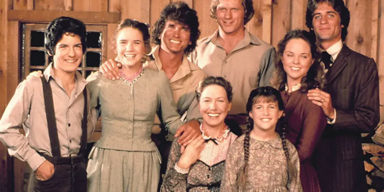 Die Besetzung von Unsere kleine Farm: Eine glückliche Familie posiert vor einer Holzwand.