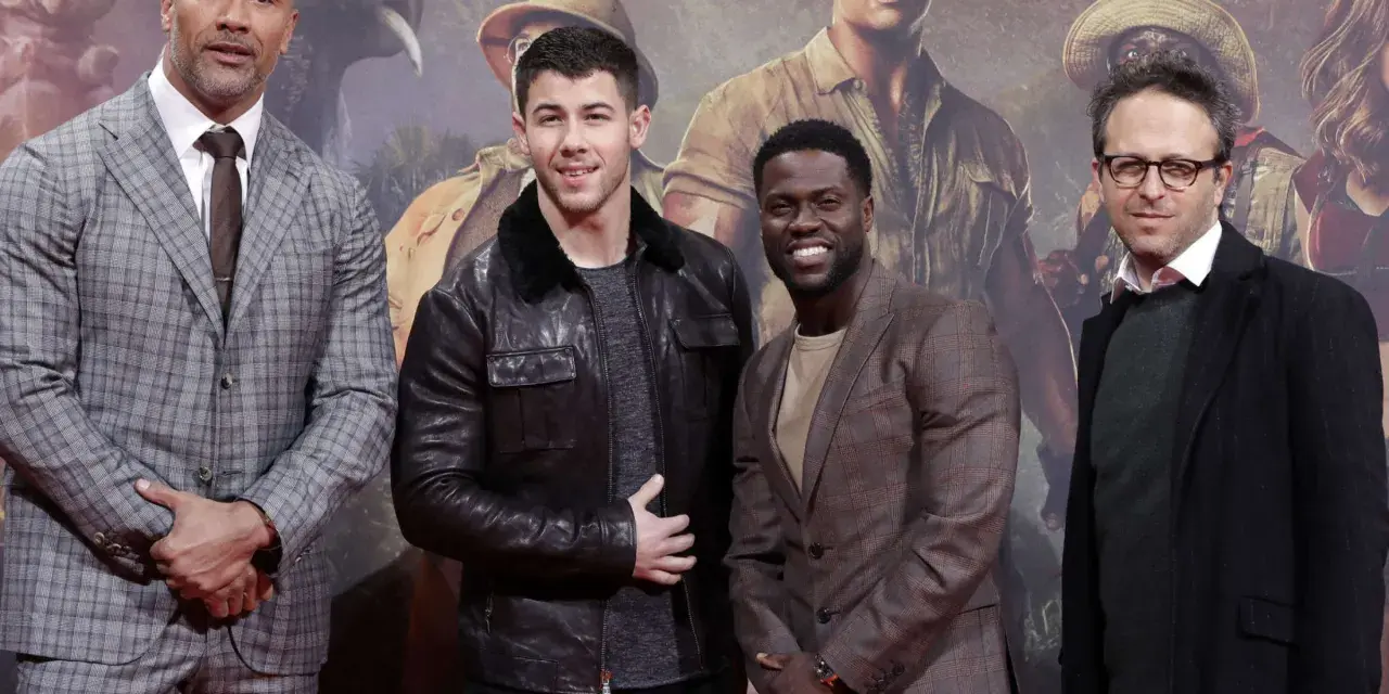 Die Besetzung von Jumanji: Dwayne Johnson, Nick Jonas, Kevin Hart und Jake Kasdan posieren vor einem Dschungel-Hintergrund.