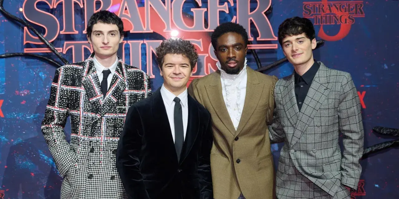 Die Besetzung von Stranger Things posiert vor dem Logo der Serie.