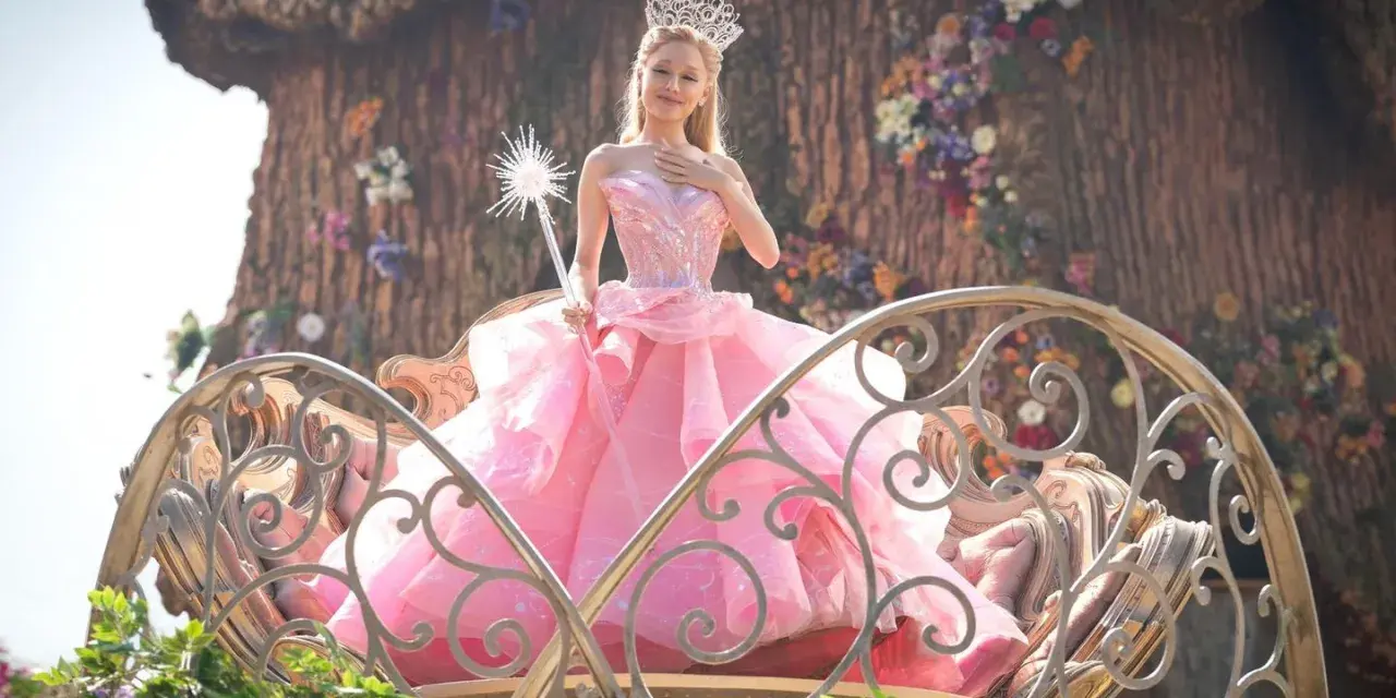 Ariana Grande als Glinda im Film "Wicked", in einem rosa Ballkleid und mit Zauberstab.