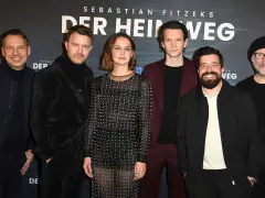 Das Ensemble des Films "Der heimweg" posiert lächelnd vor dem Banner.