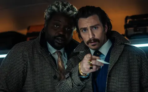 Aaron Taylor-Johnson und Brian Tyree Henry, Teil der Besetzung von Bullet Train, blicken ernst in die Kamera, während sie sich auf einem Zugabteil gegenüberstehen.