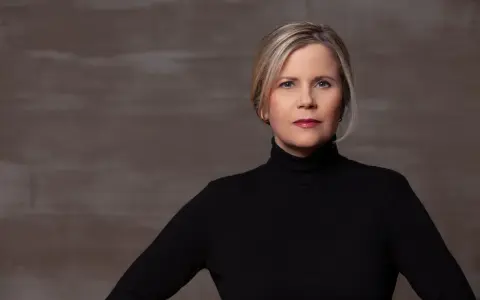 Porträt einer Frau mit blonden Haaren und einem schwarzen Rollkragenpullover. Sie könnte eine Schauspielerin sein, die in **Filme von Michaela Schaffrath** mitspielt.