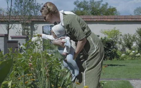 Frau mit Baby im Garten vor blühenden Blumen.