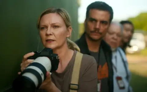 Kirsten Dunst mit Kamera, Teil der besetzung von Civil War, im Hintergrund unscharfe Personen.
