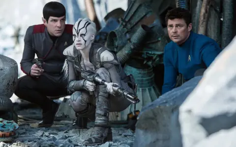 Die Besetzung von Star Trek 2009: Spock, eine Kriegerin mit Kriegsbemalung und Dr. McCoy kauern im Trümmerfeld.