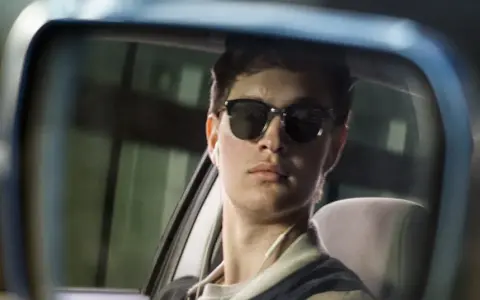 Ein junger Mann mit Sonnenbrille und Kopfhörern im Rückspiegel, der an die Besetzung von Baby Driver erinnert.