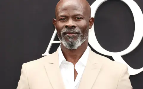 Djimon Hounsou, bekannt aus vielen Filmen, trägt einen hellbeigen Anzug und ein weißes Hemd.