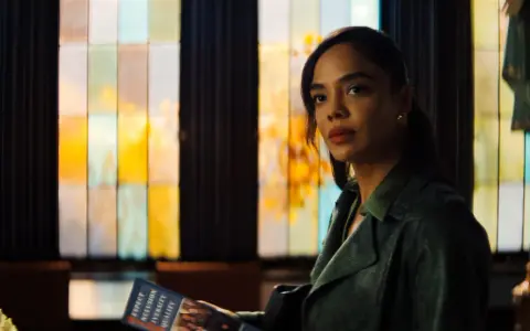 Tessa Thompson in einem grünen Mantel, mit einem Heft in der Hand, vor einem bunten Fenster. Ein Blick auf ihre Rolle in Filmen von Tessa Thompson.