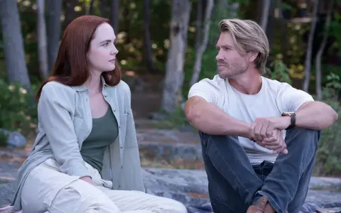 Ein Mann und eine Frau sitzen im Wald und schauen sich an. Sie sind Charaktere aus Sullivan's Crossing Staffel 4.