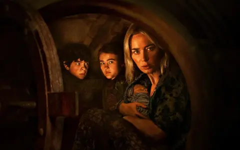 Die Besetzung von A Quiet Place: Eine Mutter hält ihr Baby, während ihre Kinder ängstlich in einem dunklen Versteck kauern.