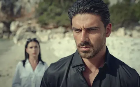 Michele Morrone, bekannt aus Filmen wie "365 Days", blickt nachdenklich in die Ferne, während eine Frau im Hintergrund steht.