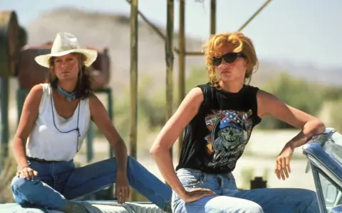 Die besetzung von Thelma & Louise: Geena Davis mit Cowboyhut und weißem Top, Geena Davis mit Sonnenbrille und schwarzem Shirt mit Totenkopf.