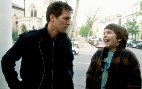 Nicholas Hoult lacht mit einem Mann auf der Straße. Ein Ausschnitt aus seinen Filmen und Serien.