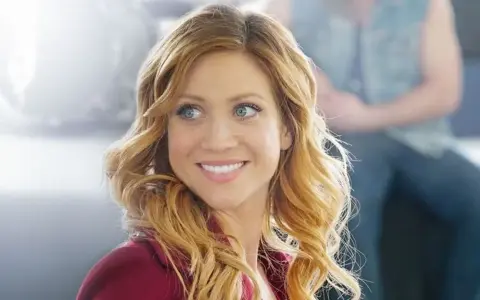 Brittany Snow lächelt in einem roten Blazer. Ein Blick auf ihre Rolle in Filmen von Brittany Snow.