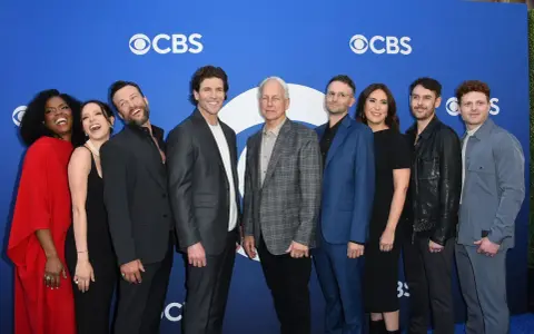 Die Besetzung von Navy CIS: Origins posiert auf einem blauen Teppich vor dem CBS-Logo.