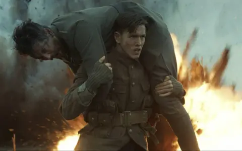 Harris Dickinson trägt einen verwundeten Kameraden durch Explosionen. Ein dramatischer Moment aus seinen Filmen.